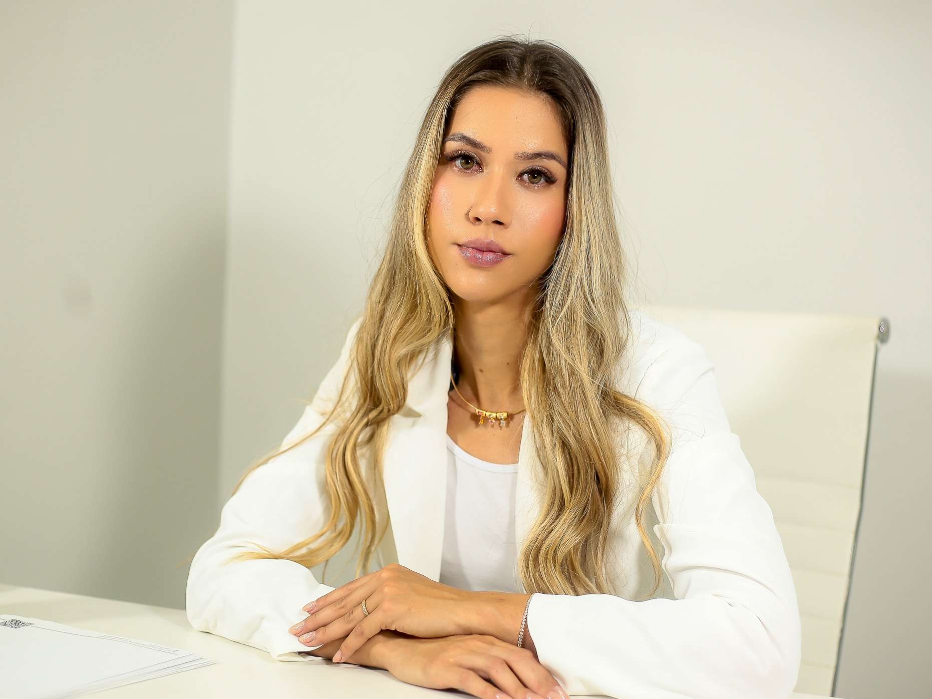 Dra. Alice Fortes de blazer branco, à mesa do consultório, olhando para a câmera.
