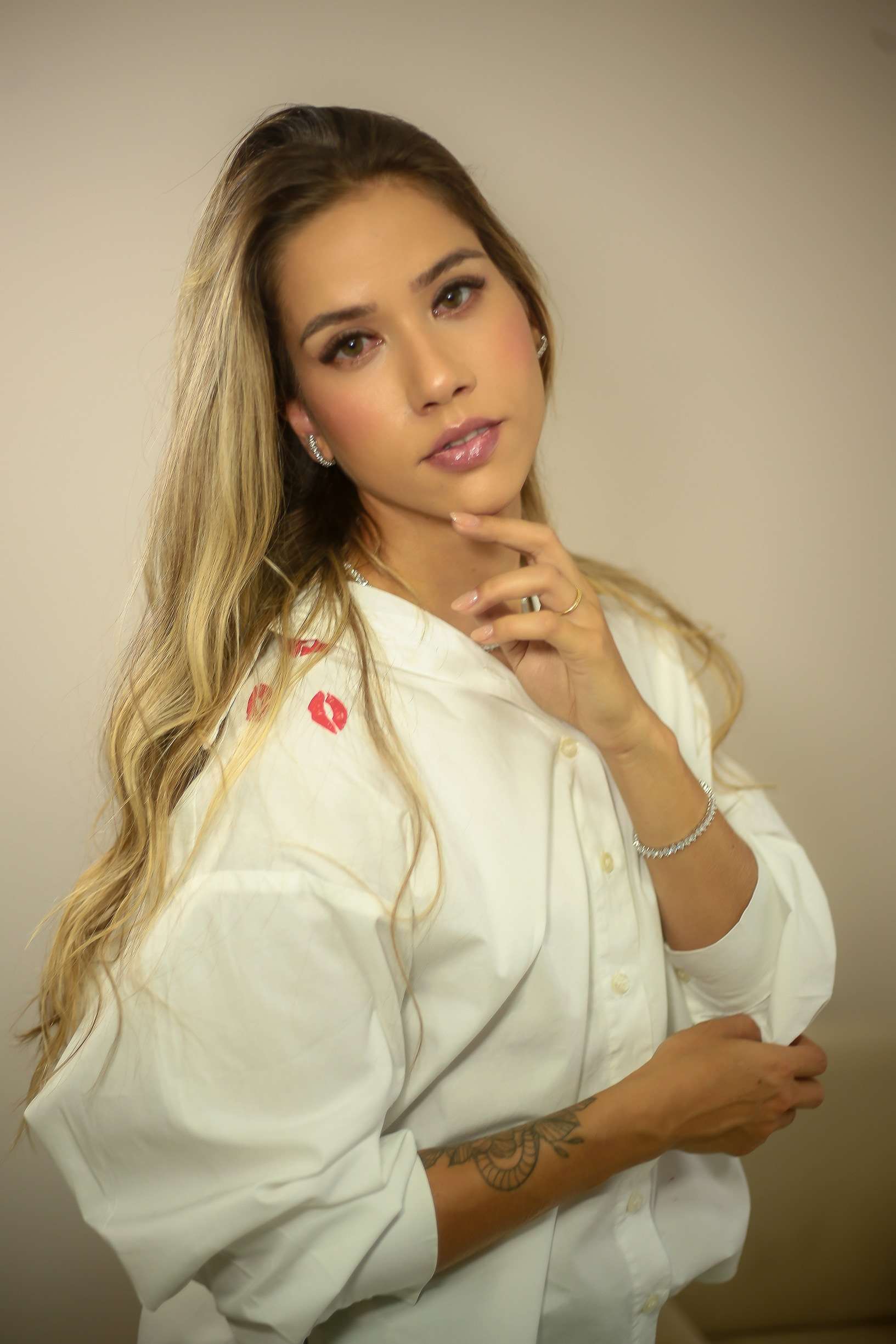 Dra. Alice Fortes de camisa branca com estampa de beijos, com a mão no queixo.