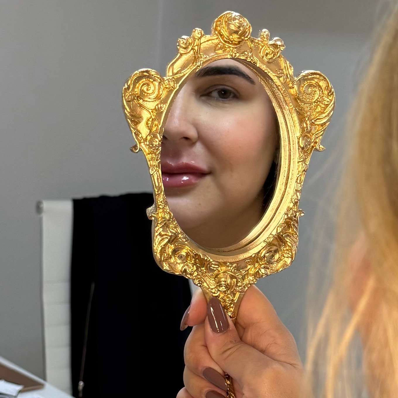 Uma paciente segura um espelho de mão dourado que reflete o rosto dela.