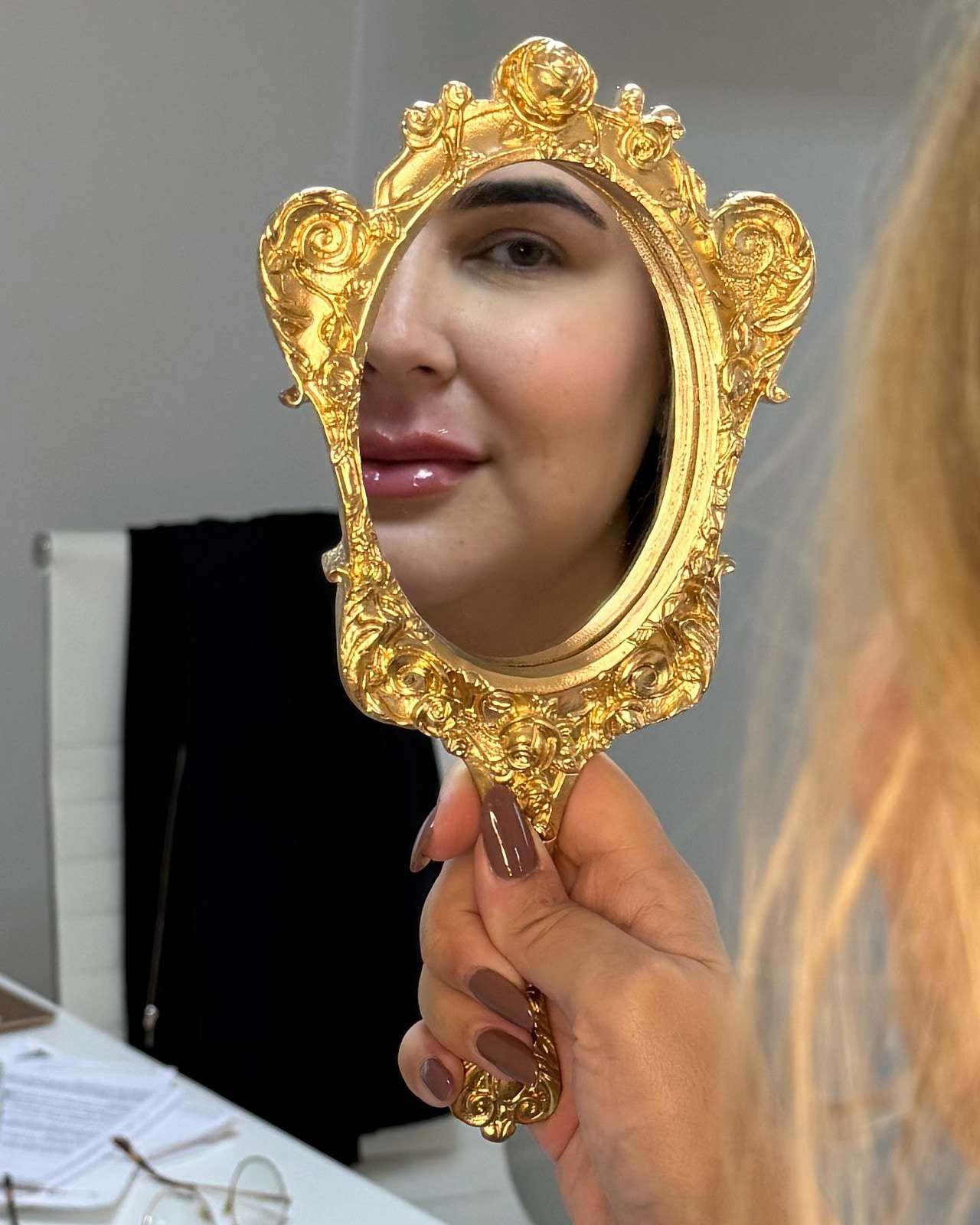 Uma paciente segura um espelho de mão dourado que reflete o rosto dela.